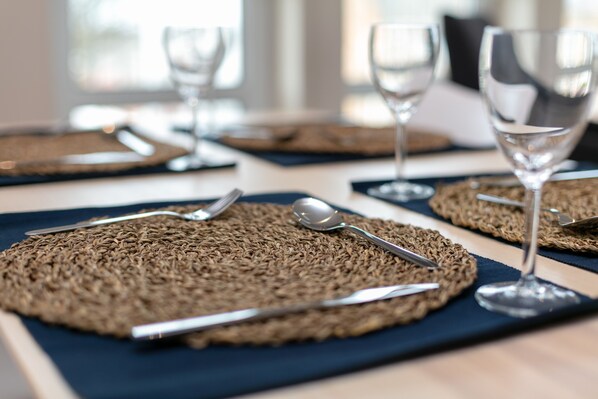 A table set with woven placemats, cutlery, and wine glasses.