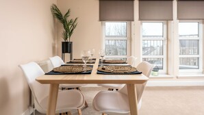 A dining area with a table set for four, white chairs, and a potted plant. - The Lucas - Donnini Apartments (Ayr)