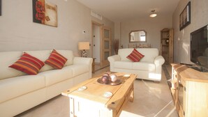 Un salon avec deux canapés blancs, une table basse en bois et un téléviseur posé sur un meuble en bois.