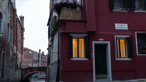Un canale stretto con un ponte, un edificio rosso con un cartello 'Corte Borella' e una barca sullo sfondo.