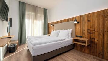 A modern hotel room with a large bed, wooden paneling on the walls, a desk with a chair, and a TV mounted on the wall.