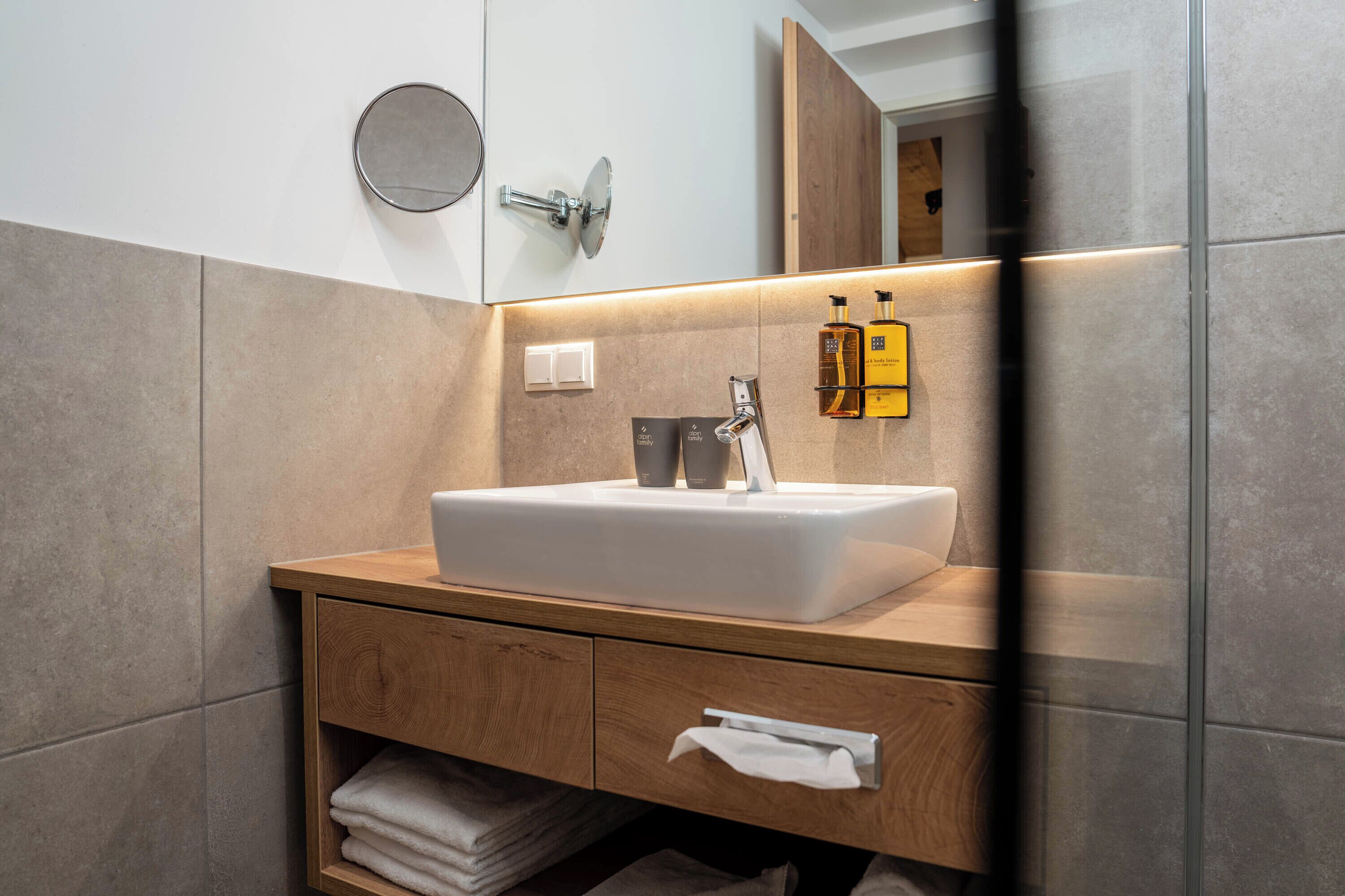 A modern bathroom with a white sink, wooden vanity, and a mirror above.