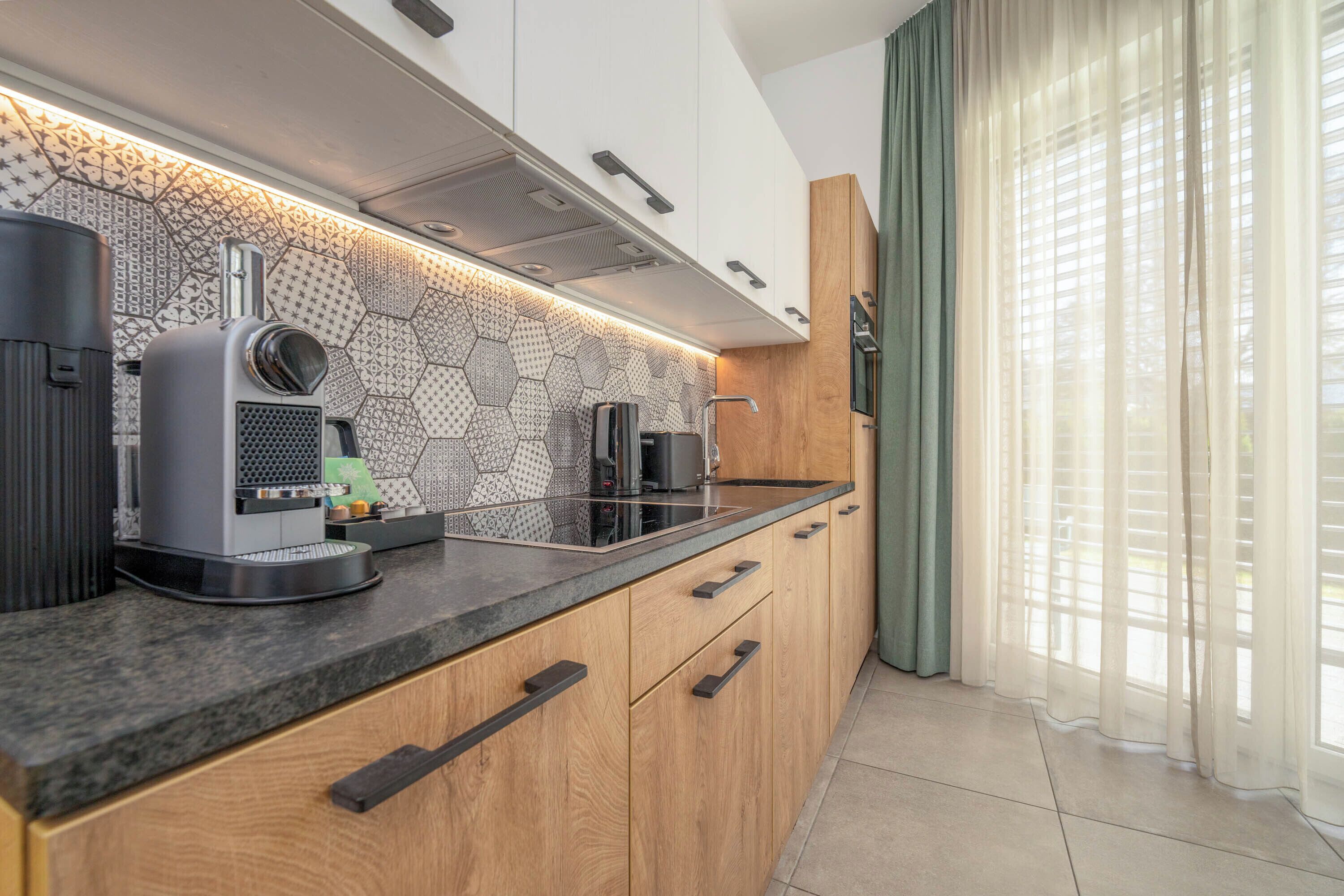 A modern kitchen with a hexagonal backsplash, a built-in coffee machine, and wooden cabinets.