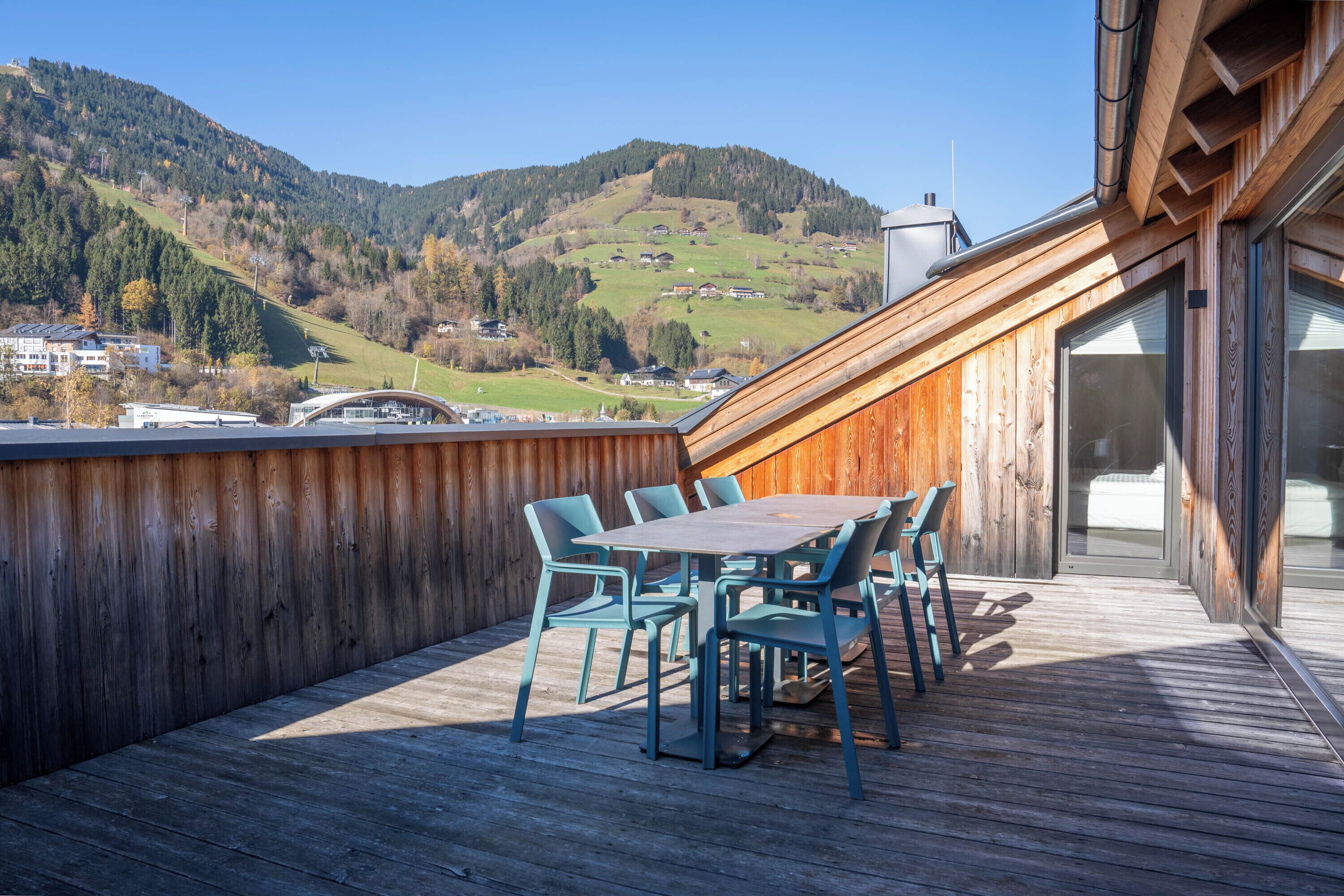A wooden deck with a table and chairs, overlooking a mountainous landscape.