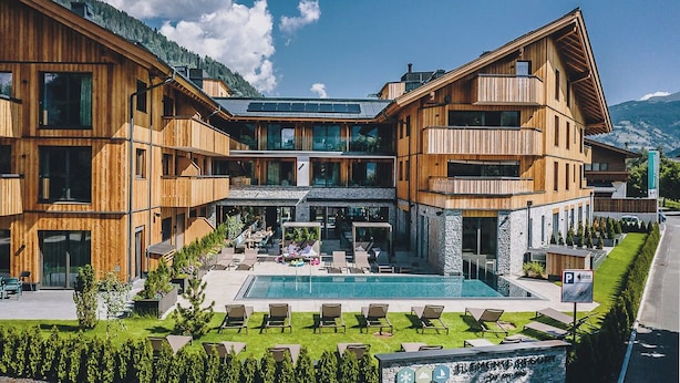 Un edificio moderno de madera con piscina, mobiliario exterior y un letrero que indica que es un hotel.