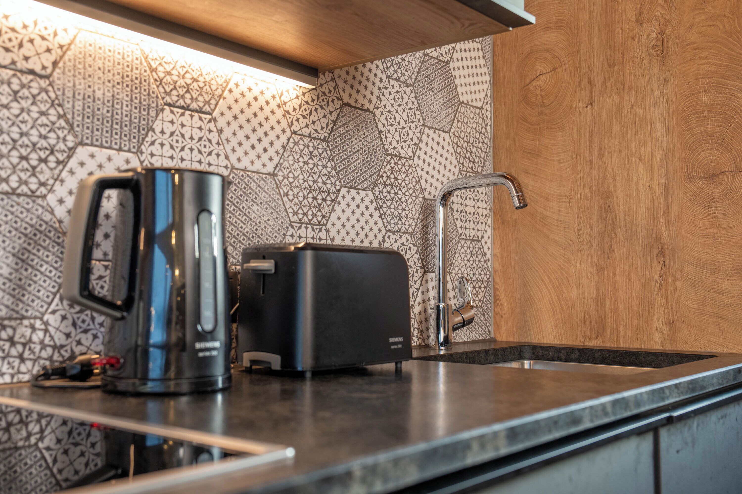 A kitchen with a modern design, featuring a patterned backsplash, a black coffee maker, a toaster, and a stainless steel sink.