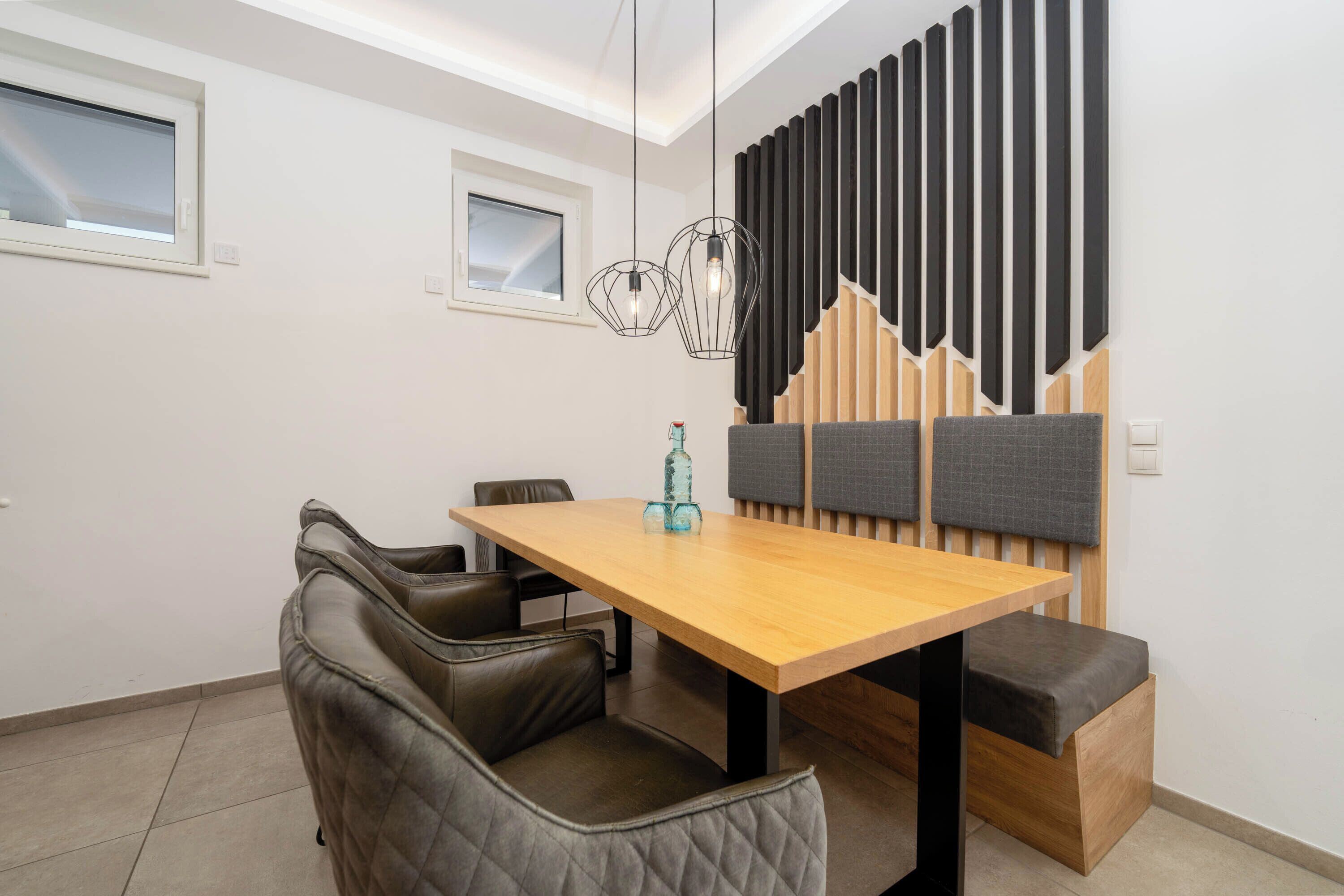 A modern dining area with a wooden table, leather chairs, and a soundproofing panel on the wall.