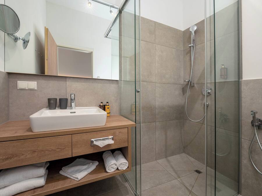 Un baño moderno con ducha envuelta en cristal, tocador de madera con lavamanos y un espejo.
