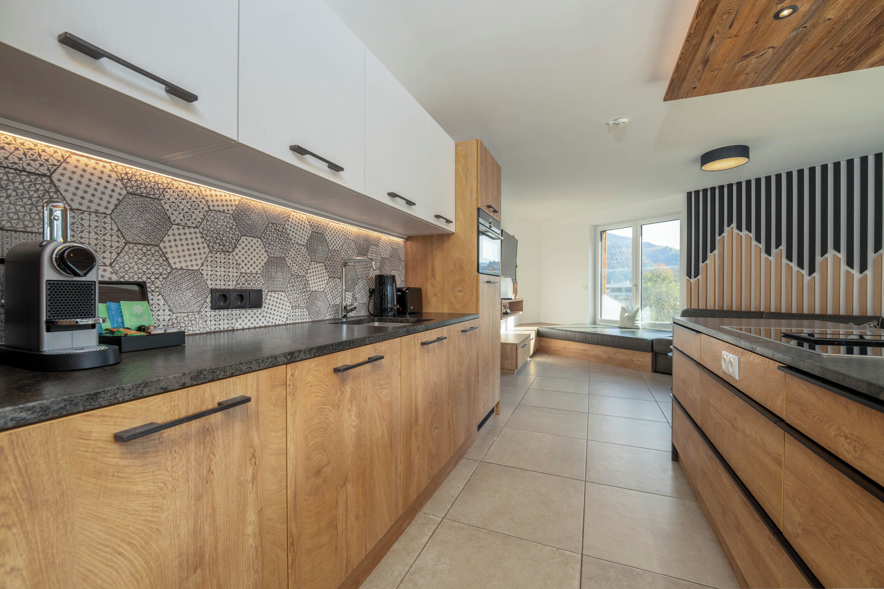 A modern kitchen with wooden cabinets, a black countertop, and a hexagonal patterned backsplash.