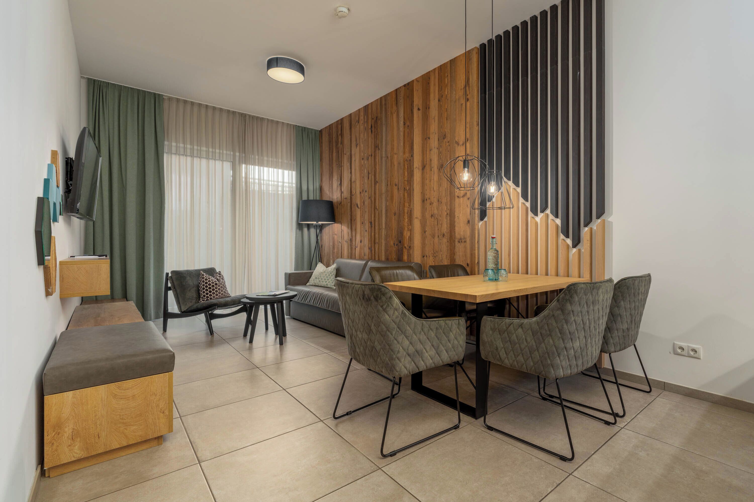 Una sala de estar moderna con una pared de acento de madera, un comedor con mesa y sillas de madera, un sofá, un televisor montado en la pared y una lámpara.