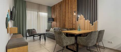 Una sala de estar moderna con una pared de acento de madera, un comedor con mesa y sillas de madera, un sofá, un televisor montado en la pared y una lámpara.