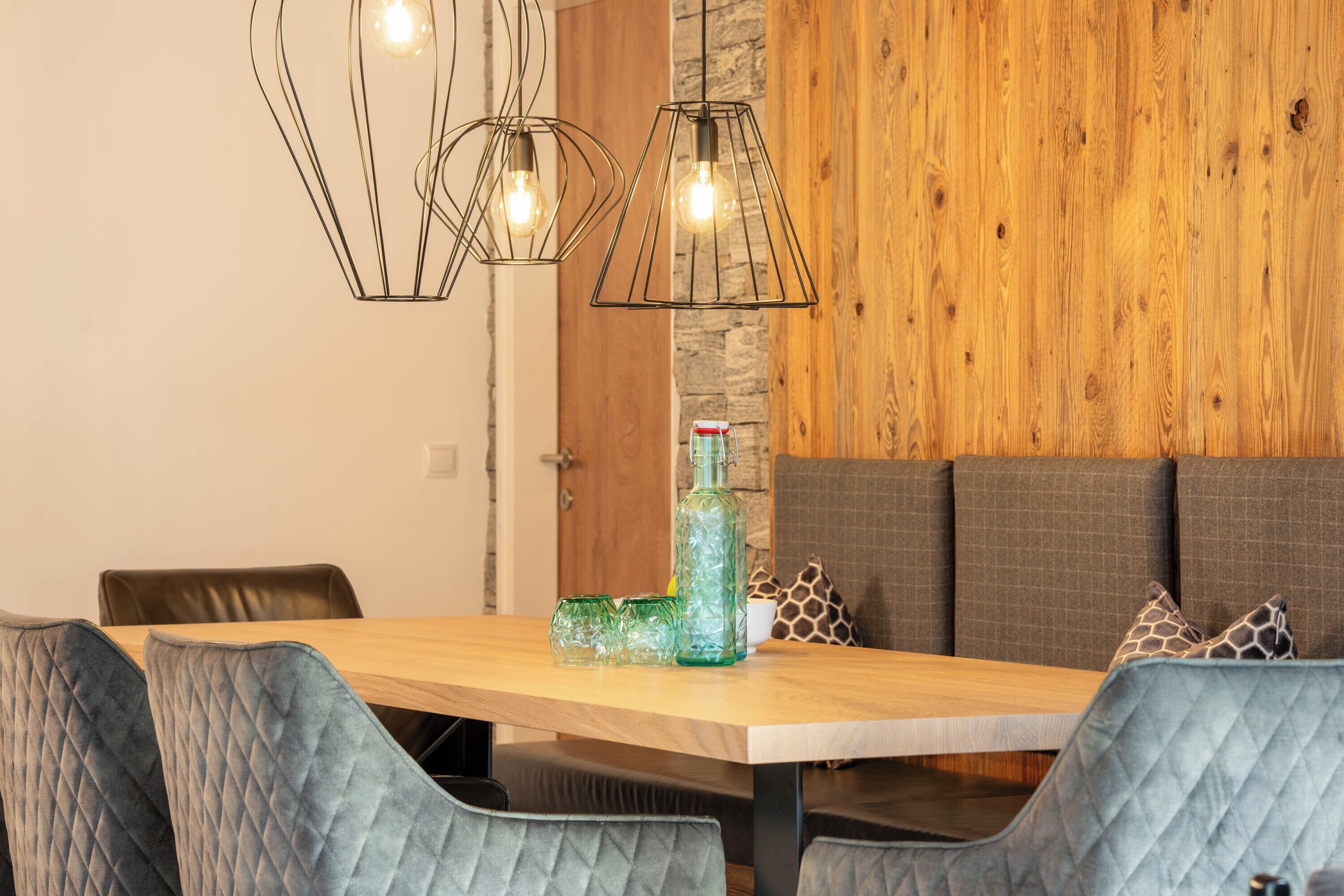 A dining area with a wooden table, cushioned chairs, and pendant lights.