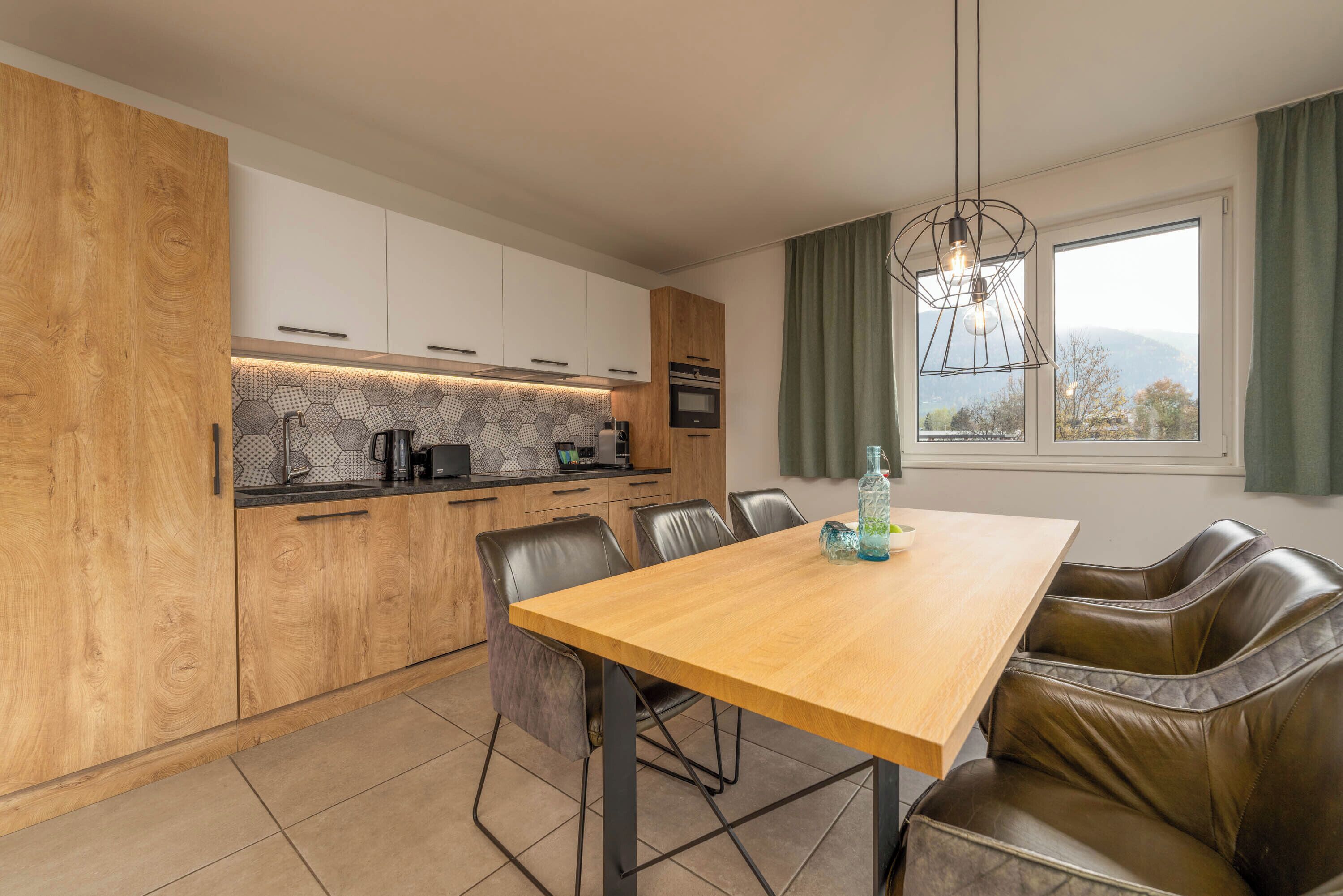 A modern kitchen with wooden cabinets, a dining table, and leather chairs.