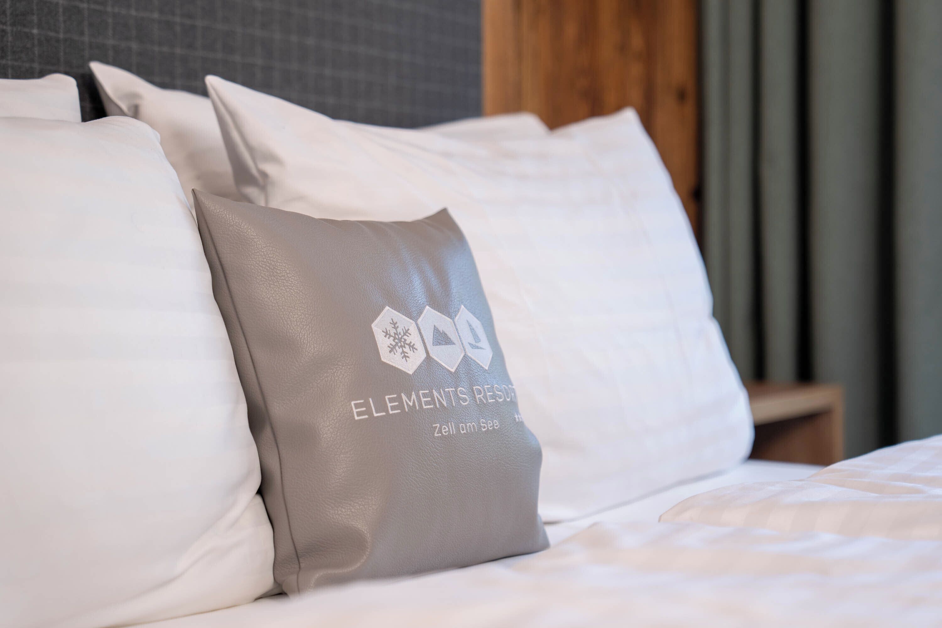 A bed with white and gray pillows, one with a logo and text.