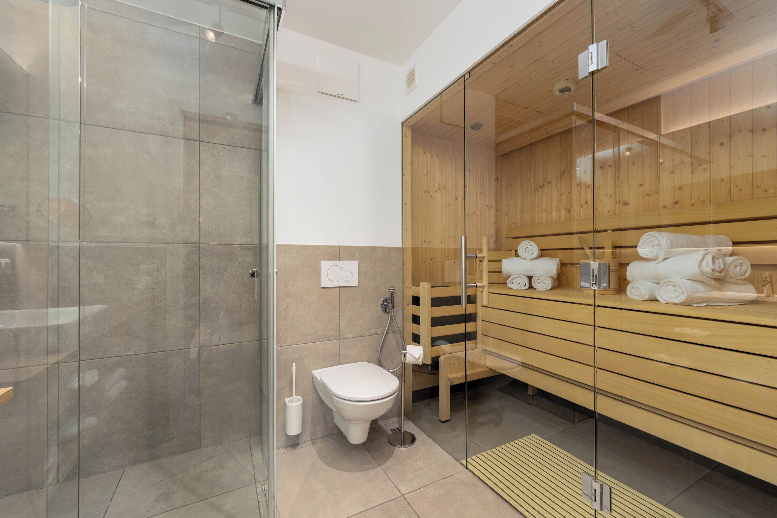 Ein modernes Badezimmer mit Duschkabine aus Glas, einem Holz-Saunabereich und einer Toilette.