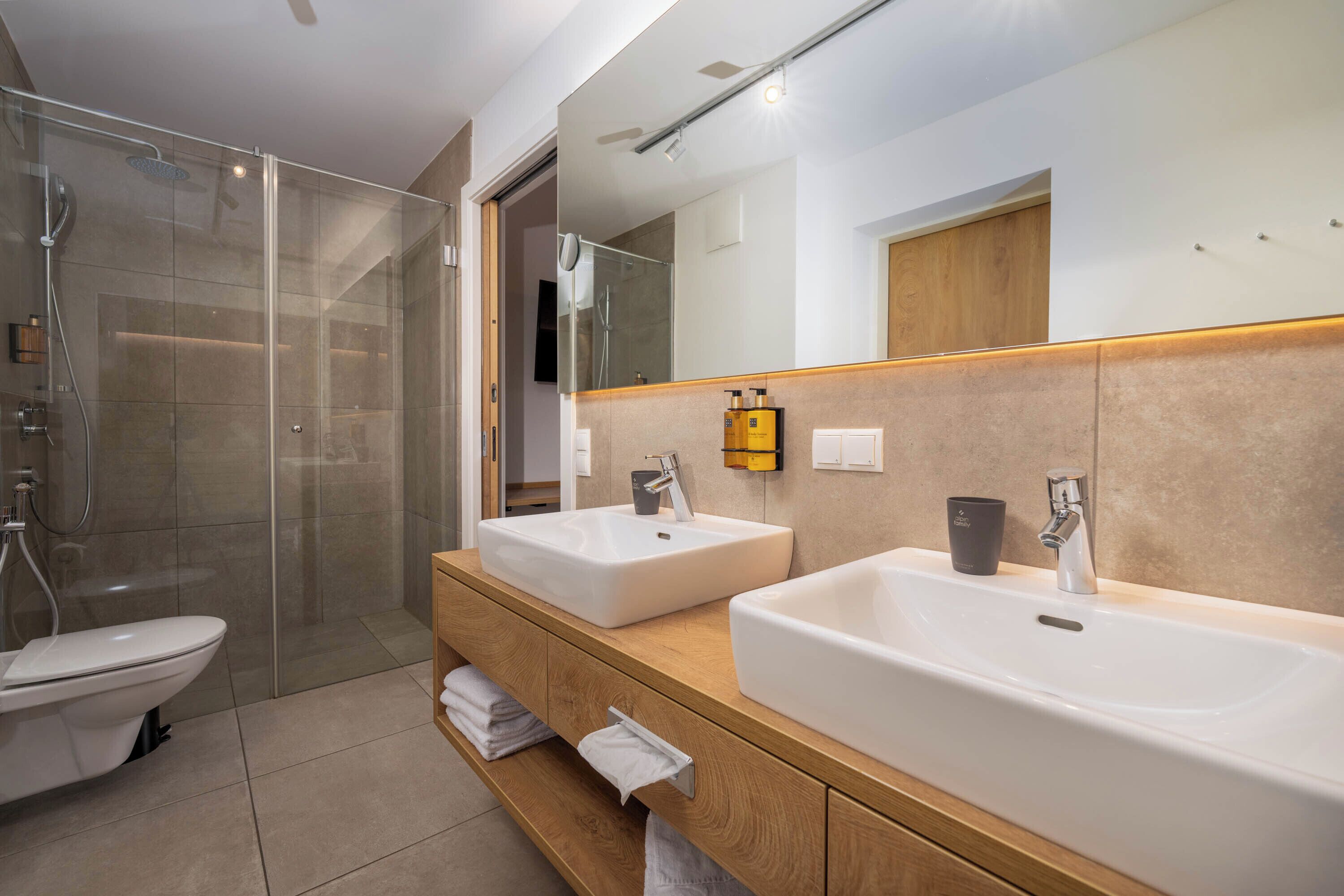 Un baño moderno con ducha de vidrio, dos lavamanos y un espejo grande.