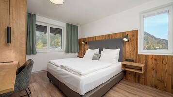 Een moderne slaapkamer met een groot bed, een houten hoofdbord, een bureau en uitzicht op een bebost gebied.