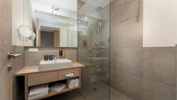 Une salle de bain moderne avec une douche à parois de verre, un grand miroir et un meuble-lavabo en bois doté d’un évier et d’un espace de rangement pour les serviettes.