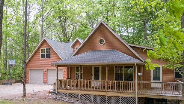 Een houten chalet met twee verdiepingen, een overdekte veranda en een garage.