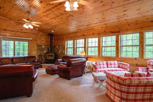 A log cabin interior with a fireplace, leather sofas, plaid couches, and large windows. - Spacious Floradale Retreat w/ shared heated Pool, Tennis + more. Close to dunes! (Mears)
