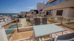 Eine Dachterrasse mit Pool, Sitzgelegenheiten im Freien und Blick auf das Meer und andere Gebäude.