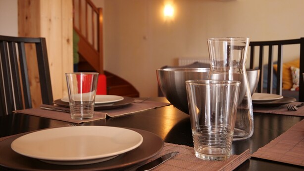 Une table à manger dressée avec des assiettes, des couverts et de la verrerie transparente.