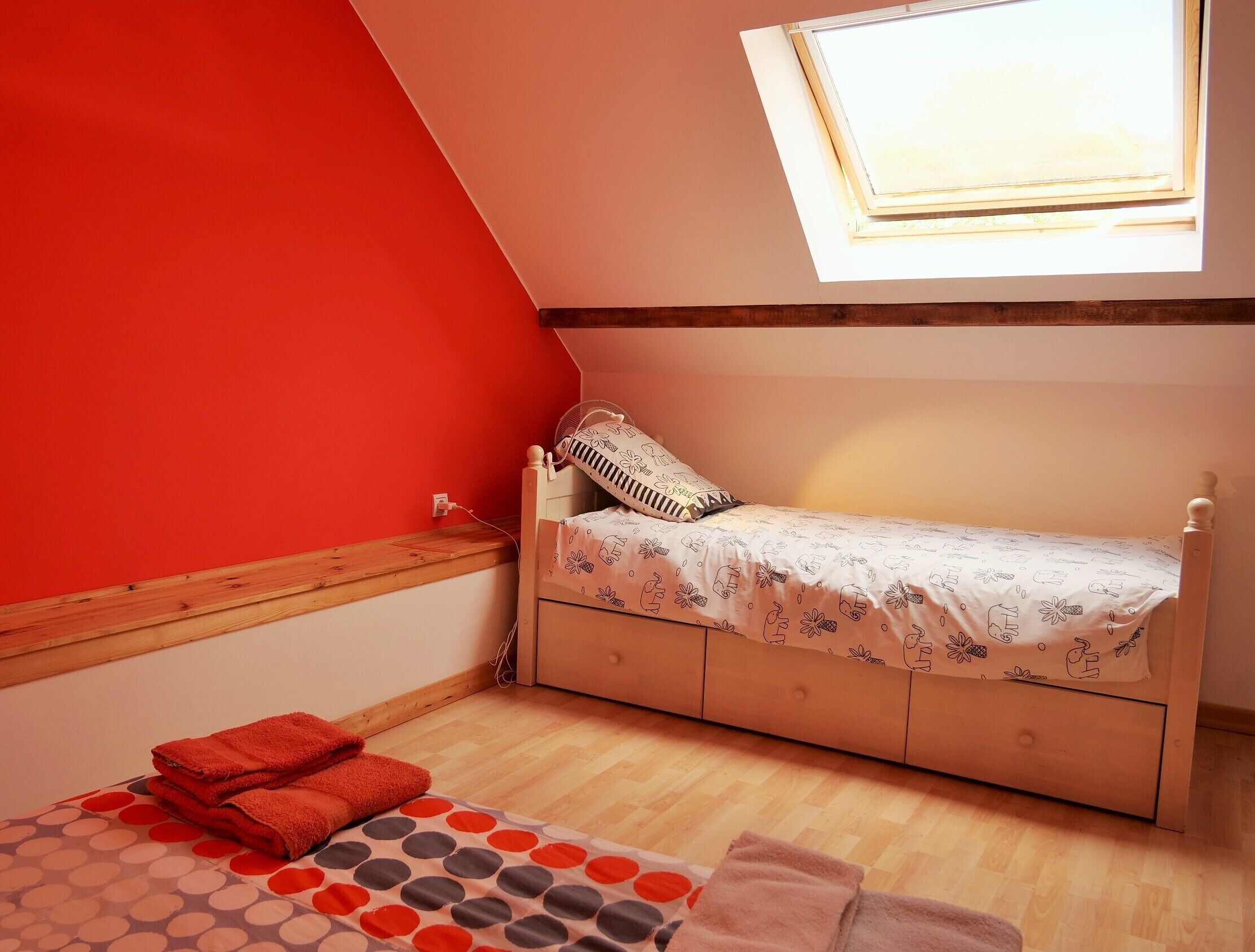 A small, cozy bedroom with a sloped ceiling, a single bed, a window, and a wooden floor.