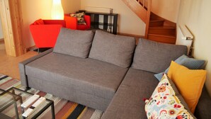 Un salon avec un canapé gris, un fauteuil rouge, une table basse en verre et un escalier.