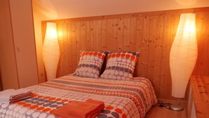 Un lit bien fait, avec une literie à motifs, deux oreillers et une serviette orange pliée.