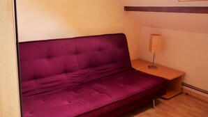 Un canapé violet dans une pièce dont le sol est recouvert de parquet, avec une lampe posée sur une table de chevet en bois.