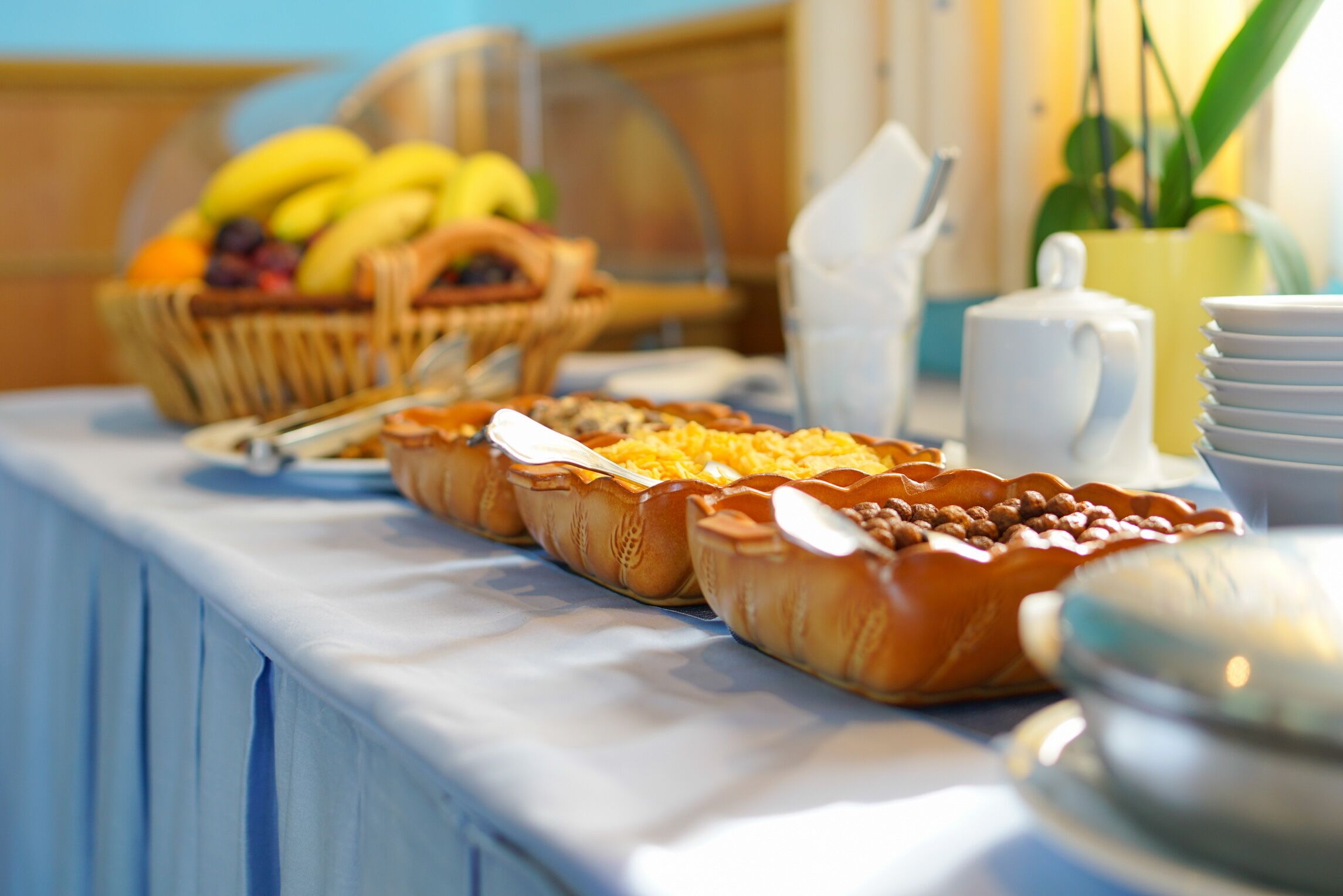A breakfast buffet with various pastries, a fruit basket, and a teapot.