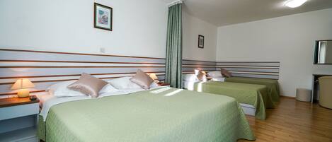 A hotel room with two beds, a green carpet, wooden flooring, and a nightstand with a lamp.