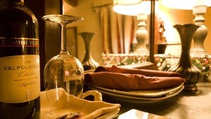 A bottle of Valpolicella wine, a wine glass, and a table setting with plates and napkins. - Villa Gesi - Apartment 3 (Negrar)