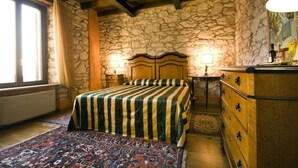 A bedroom with a stone wall, wooden bed, two bedside lamps, a dresser, and a patterned rug. - Villa Gesi - Apartment 3 (Negrar)