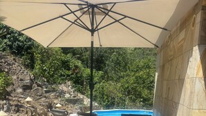 Eine Terrasse im Freien mit Korbmöbeln, einem Tisch mit kariertem Tischläufer und einem Pool im Hintergrund.