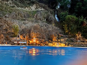 Une piscine bordée de rochers, une cascade et des structures illuminées.