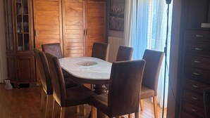 Ein Essbereich mit einem runden Tisch, sechs Stühlen, Holzschränken und einem Heizkörper nahe eines Fensters.