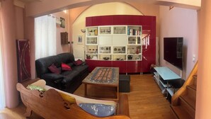 Ein Wohnzimmer mit einem schwarzen Ledersofa, einer Holzbank, einem Couchtisch, einem roten Schrank mit Regalen und einem Fernseher.