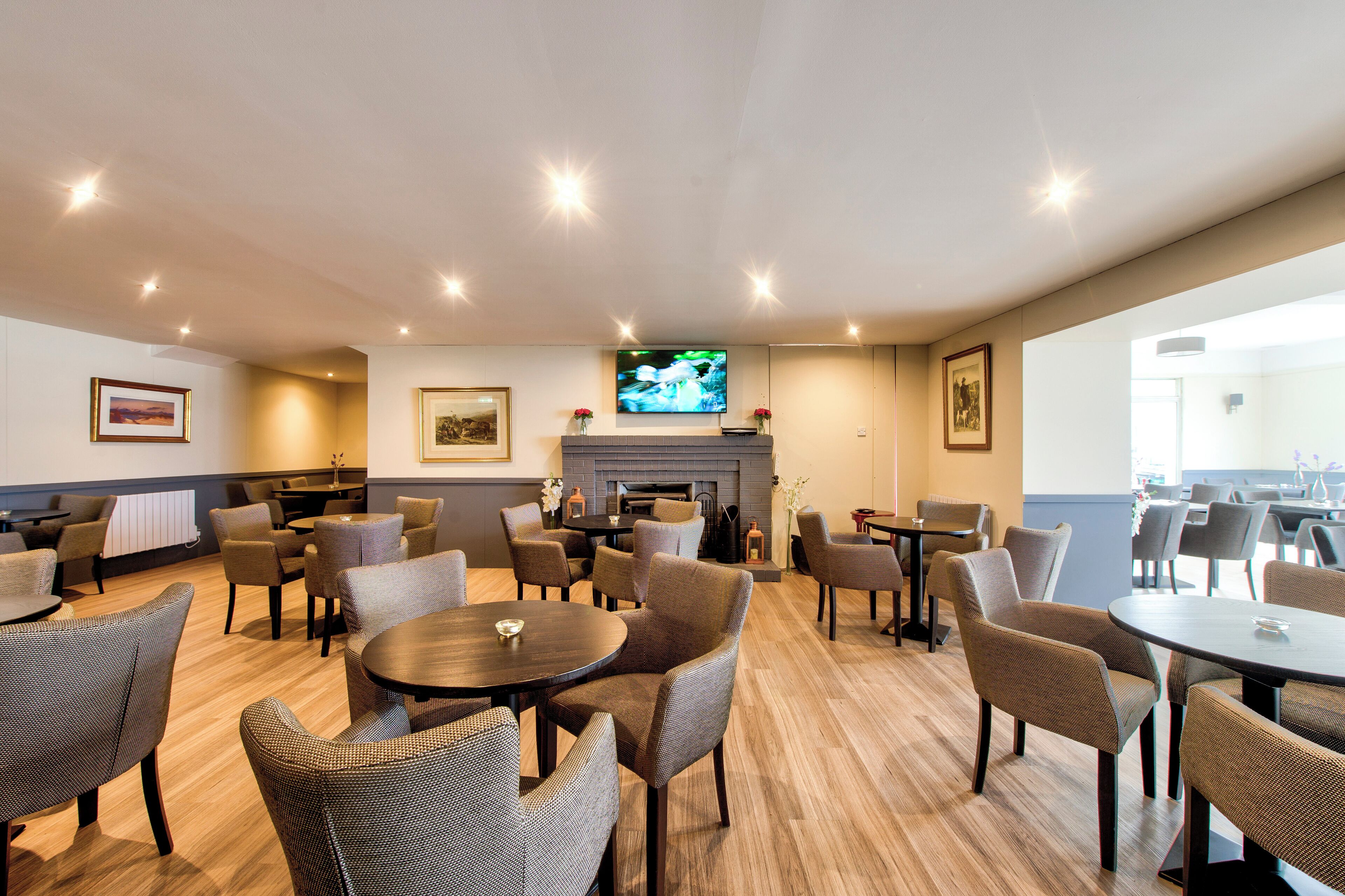 A spacious lounge area with multiple seating arrangements, a television mounted on the wall, and a fireplace.