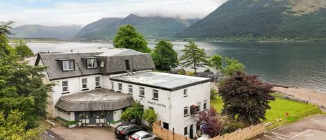 A hotel with a white facade, a parking area, and a view of a lake and mountains.