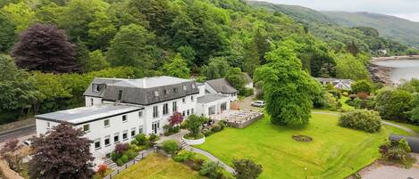 Un bâtiment blanc doté d’un toit plat, entouré d’une végétation luxuriante et bordé par une rivière.