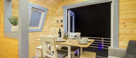 A cozy wooden cabin interior with a dining area, a sofa, and a window overlooking a dark exterior.