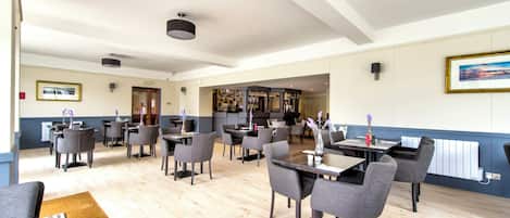 A spacious dining area with multiple tables and chairs, a bar in the background, and a view of the bar area.