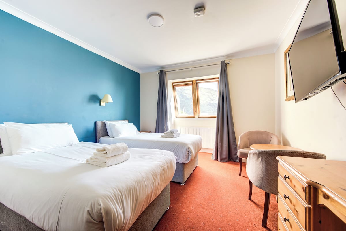 Habitación de hotel con dos camas, un aparador de madera, televisor y ventana con cortinas.