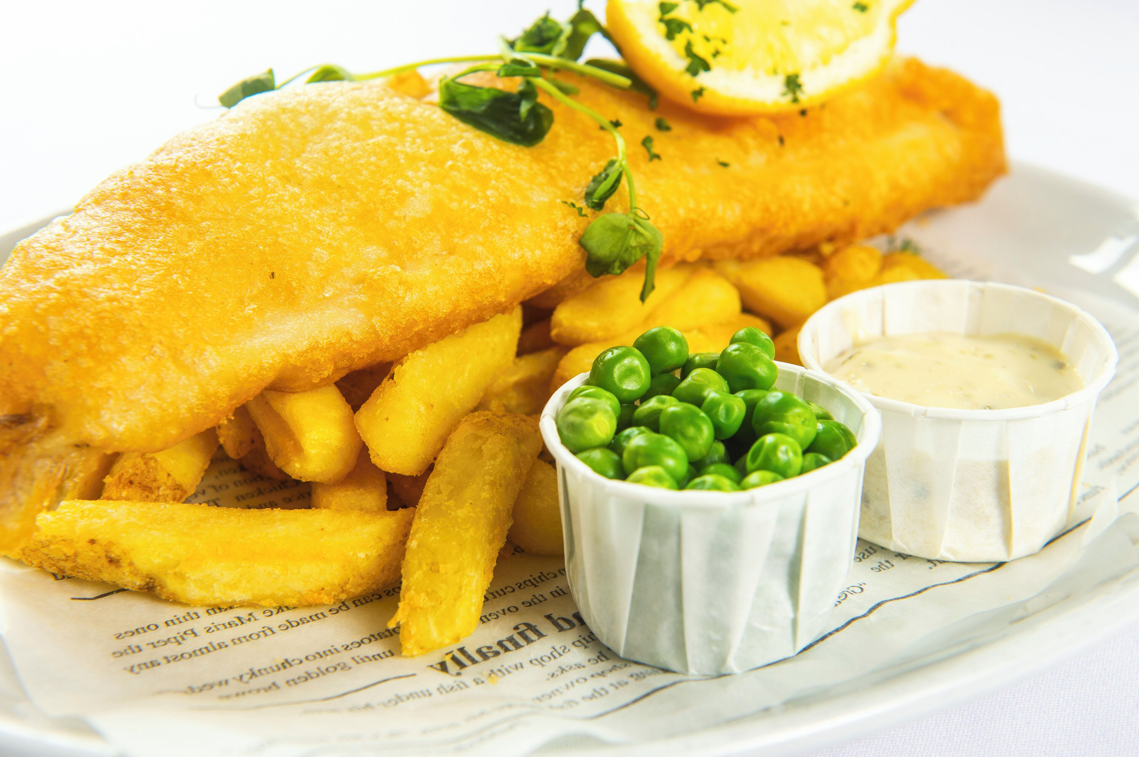A plate of fish and chips with peas and two dipping sauces.