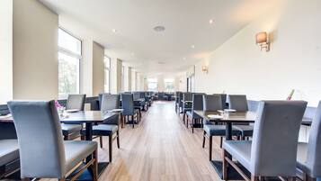 A spacious dining area with long tables and chairs, large windows, and a clean, modern design.