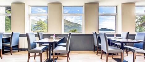 A dining area with multiple tables and chairs, large windows with a view of mountains and trees, and a modern interior design.