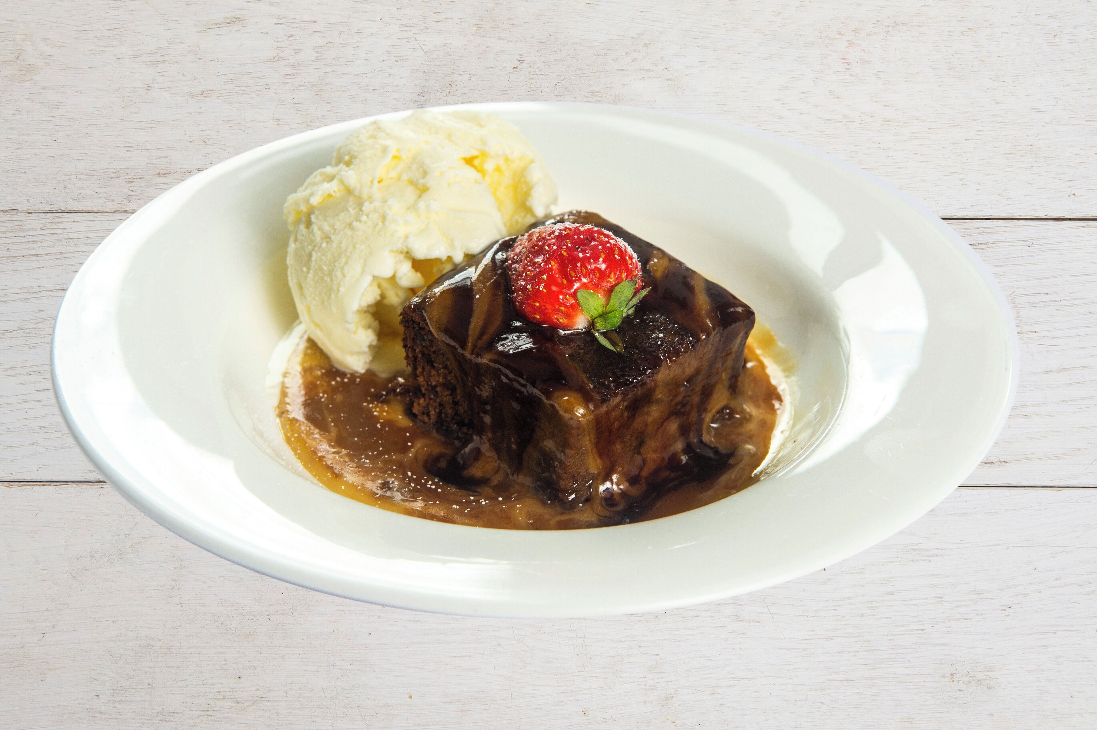 A dessert plate with a chocolate cake, a scoop of vanilla ice cream, and a strawberry on top.