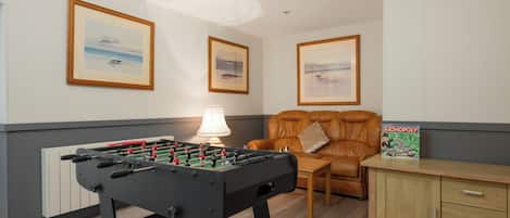 Um quarto com mesa de futebol, sofá, luminária, quadros nas paredes e um jogo de Banco Imobiliário.
