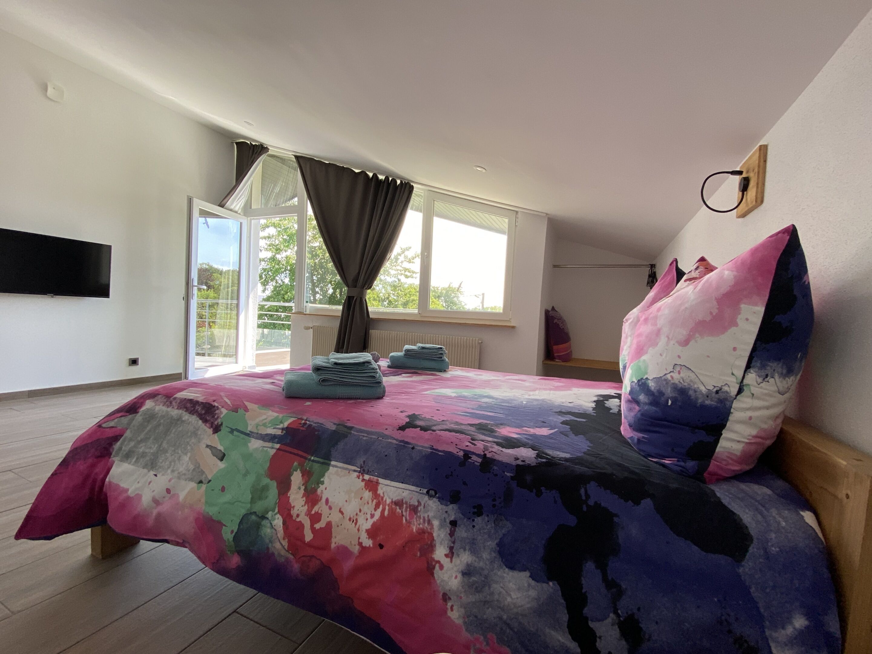 Ein Schlafzimmer mit einem großen Bett, einem an der Wand montierten Fernseher und einem Fenster mit Vorhängen.